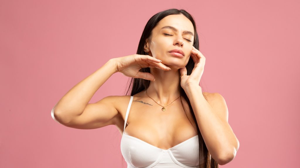 Beauty shot of healthy glowing skin showing lady portrait with hands on pink background